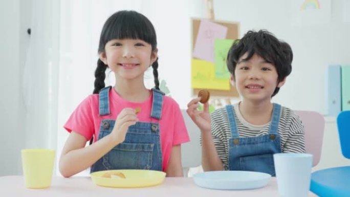 亚洲幼儿学生在餐桌上共进午餐的肖像。可爱的小学龄前女孩和男孩在幼儿园托儿所的课间休息时间感到快乐和喜