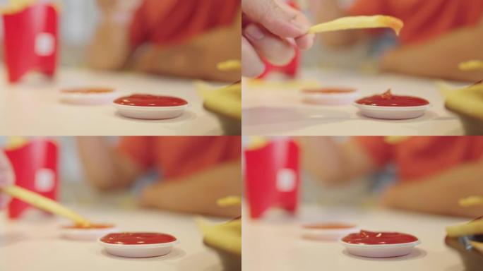 男人的手拿着炸薯条，然后将它们浸入餐桌上的番茄酱和辣椒酱的特写镜头。