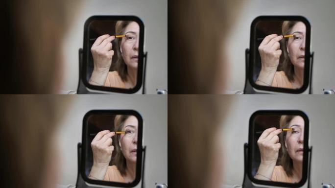 一位中年妇女看着镜子，用化妆刷在上眼睑上画上阴影。喜欢他的样子。幸福的概念，安康的，自然的美。副本的