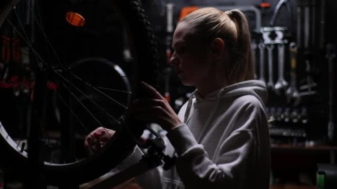专业车间黑暗车库用专用工具对准自行车车轮张力辐条的年轻美女肖像。