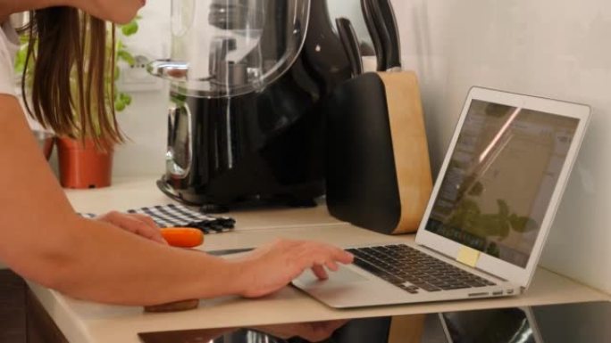 家庭主妇女商人在冠状病毒自助隔离期间，一边从厨房家庭办公室烹饪胡萝卜切片，一边工作笔记本电脑