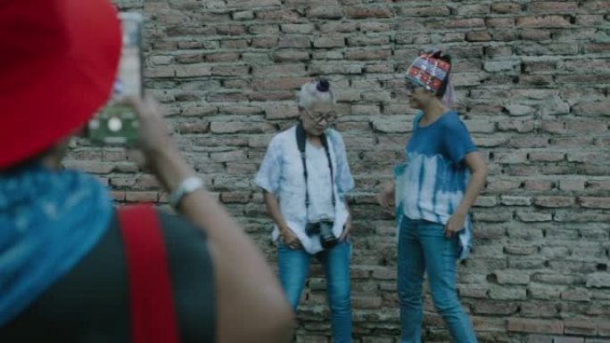 可爱的退休朋友在匹配的领带染色当地衬衫和兰纳帽子，拍摄与古墙背景的照片。
