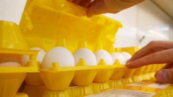 特写一个黄色塑料包装的鸡蛋和两名男子的手打开它检查鸡蛋的完整性，然后把它