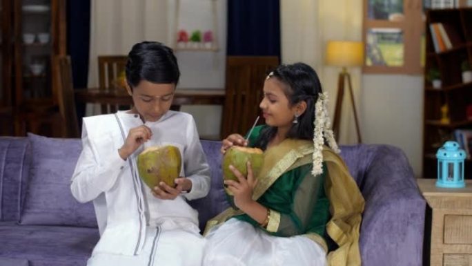 一个快乐的印度兄弟姐妹喝嫩椰子-夏天，一种清凉的饮料，传统的南印度服饰