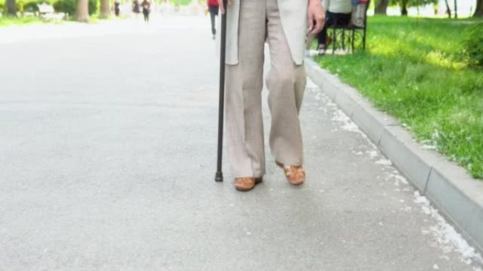 关闭在公园里用拐杖走路的高级女性腿