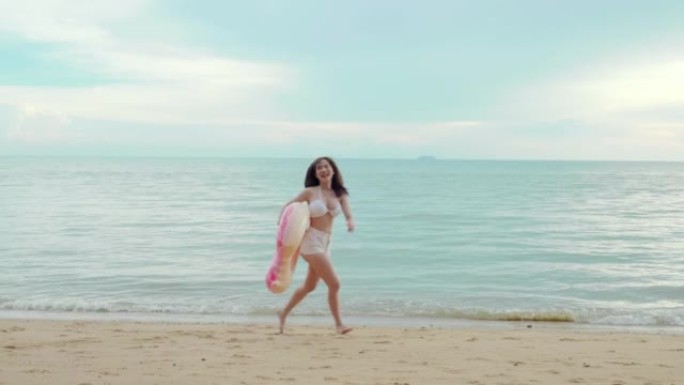 美丽的亚洲女子手持橡胶圈在沙滩上奔跑