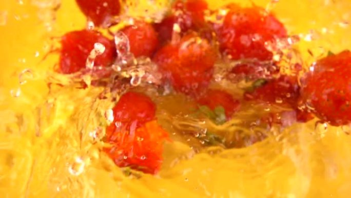 将草莓倒入橙色背景的玻璃碗中的水中。慢动作。