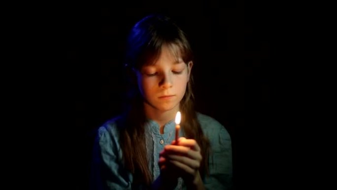 小正统女孩在黑暗的房间里手里拿着蜡烛祈祷