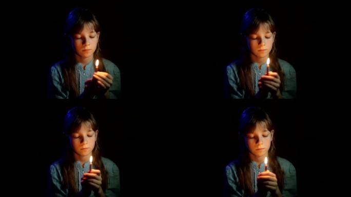 小正统女孩在黑暗的房间里手里拿着蜡烛祈祷
