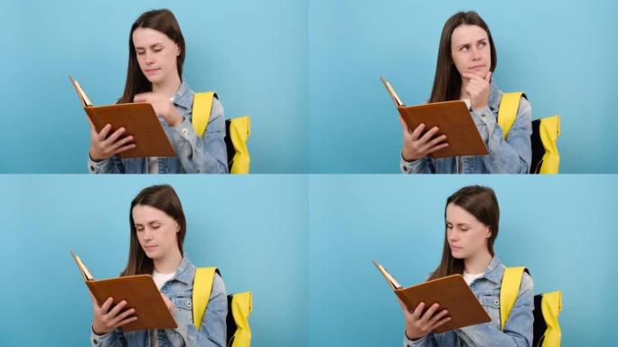 肖像女孩青少年学生穿着牛仔夹克和黄色背包看书思考梦想，在工作室的蓝色背景墙上孤立地摆姿势。高中教育大