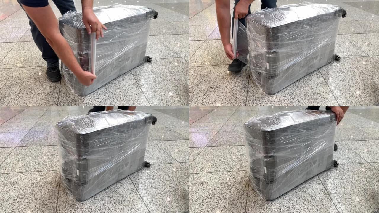 乘飞机旅行前用透明薄膜包裹手提箱的人。安全或安全保护概念。在机场航站楼打包行李
