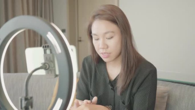 美丽的东南亚女人博主正在展示如何化妆和使用化妆品。在摄像机前在家录制vlog视频直播。社交媒体和副业