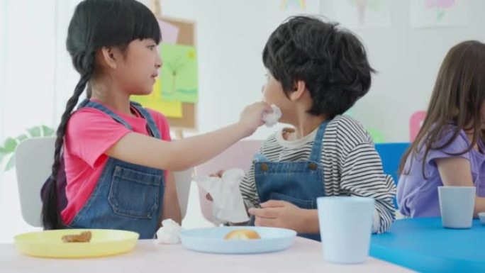 两个亚洲小孩学生一起在桌子上吃午饭。可爱的小学龄前女孩和男孩在幼儿园托儿所的教室里休息时感到快乐和喜