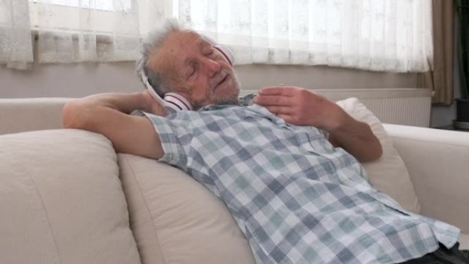 老人在家沙发上放松时，戴着耳机欣赏音乐