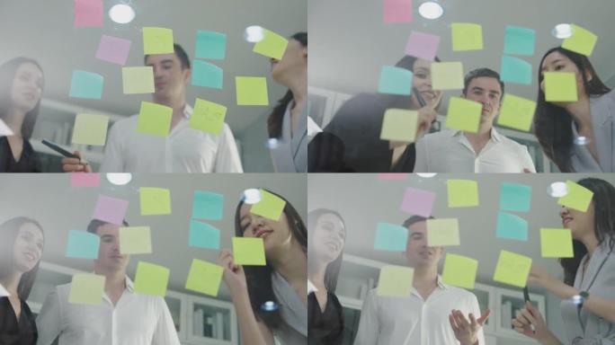 在现代办公室会议期间，启动业务团队讨论业务计划并在镜子玻璃上放置彩色便条纸