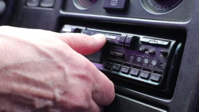 驾驶员将盒式磁带插入旧车中的盒式磁带录音机中。