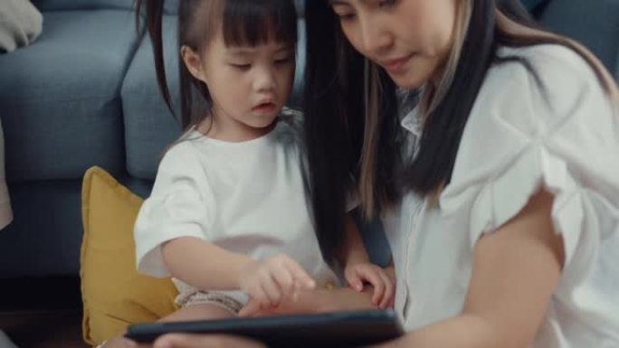 关闭年轻的亚洲父母父亲使用笔记本电脑在家工作母亲使用平板电脑玩游戏，并与女儿一起在家里的客厅看卡通电