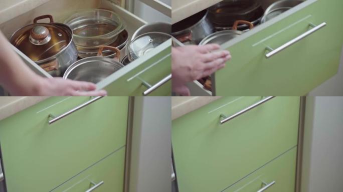 男人用手打开厨房橱柜门，在里面挨着架子拿锅。关闭带玻璃门的现代厨柜，用于存放干净的餐具