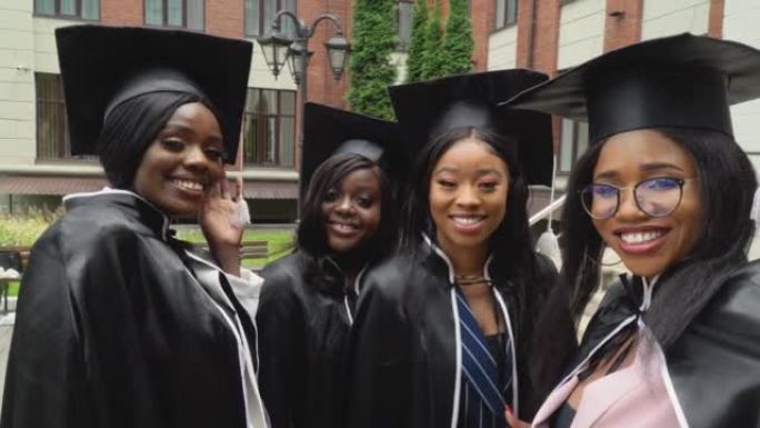 快乐的大学或大学毕业生，穿着硕士服和方帽，热闹起来，自拍。非裔美国女学生站在大学大楼附近