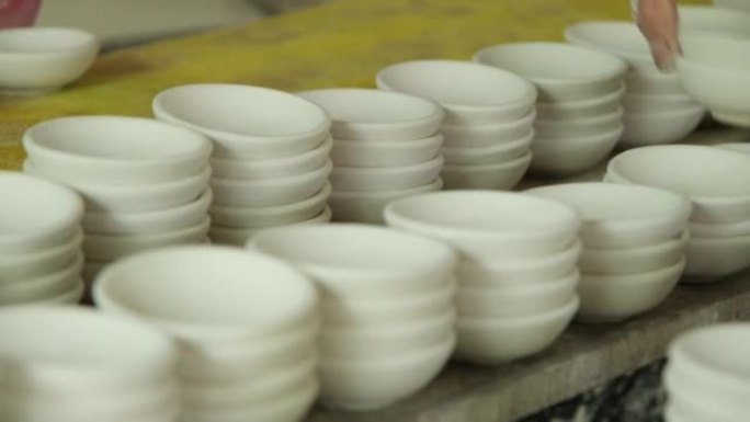许多用陶瓷粘土制成的小圆板。机架中的陶瓷杯为陶器车间表面的绘画设计做准备。手工艺和小企业概念。