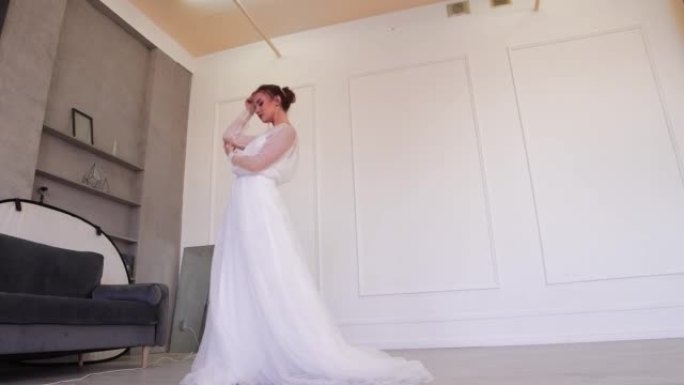 一位穿着白色连衣裙的年轻新娘站着为摄影师摆姿势。