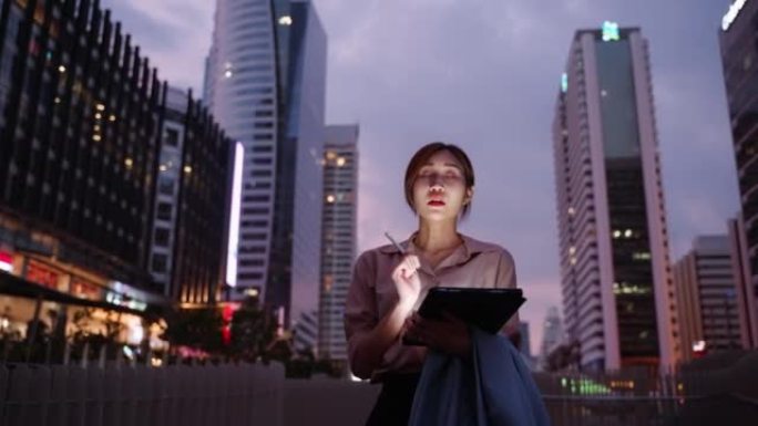 年轻女子晚上在市区散步和使用数字平板电脑