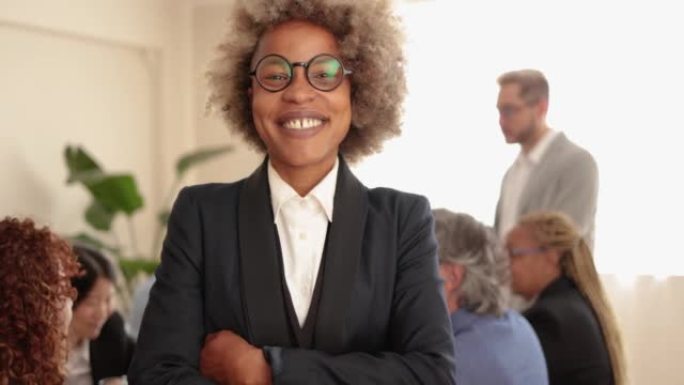 非洲女商人在与银行办公室内的同事一起工作时在镜头前微笑