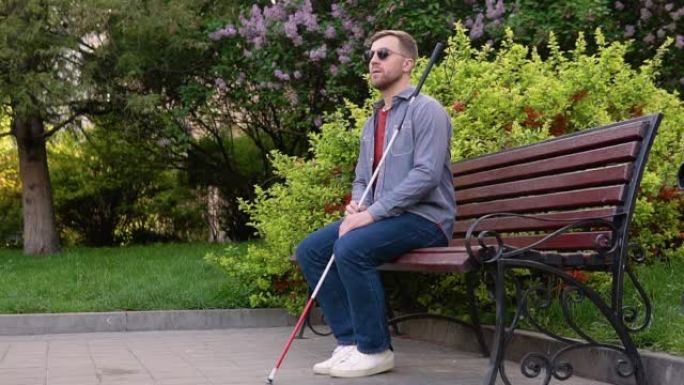 一个拐杖的盲人坐在公园的长凳上