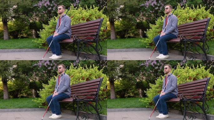 一个拐杖的盲人坐在公园的长凳上