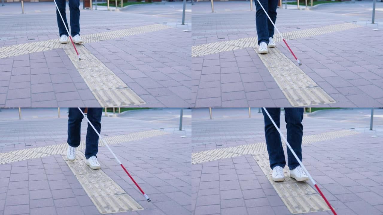 盲人的腿用手杖寻找特殊的触觉瓷砖。盲人拄着拐杖在街上行走