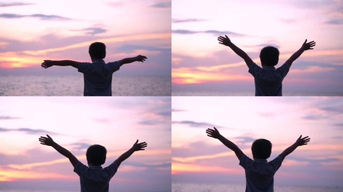 亚洲男孩举起手臂，在海滩上旋转。放松和幸福的概念