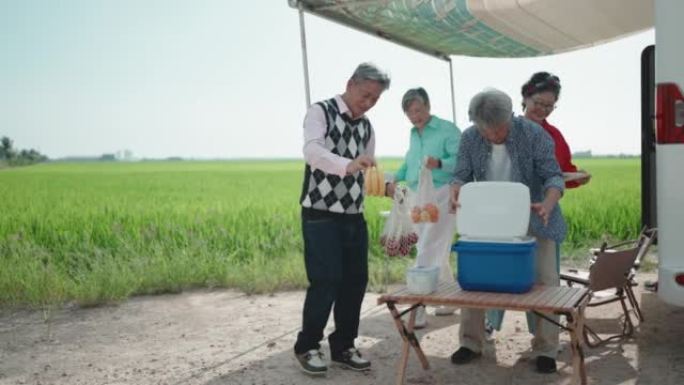 周末休闲活动期间，亚洲华人资深朋友在停在稻田的露营车旁准备晚餐