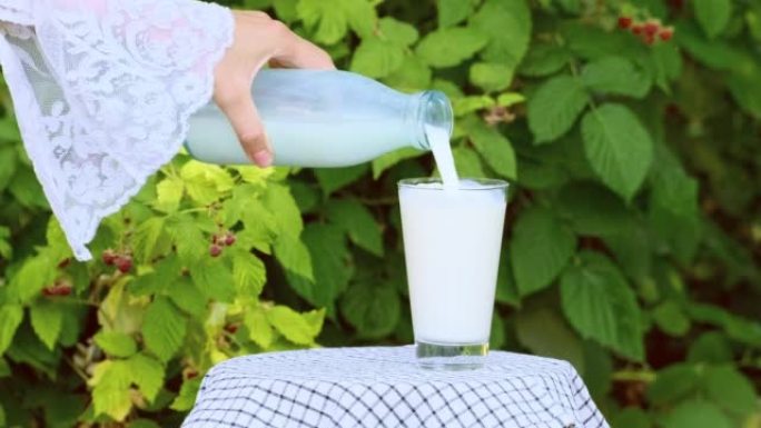 牛奶从瓶子里倒入户外的玻璃中。健康饮食的概念，有机食品和饮料的天然产物，健康的生活方式。鲜牛奶倒入玻