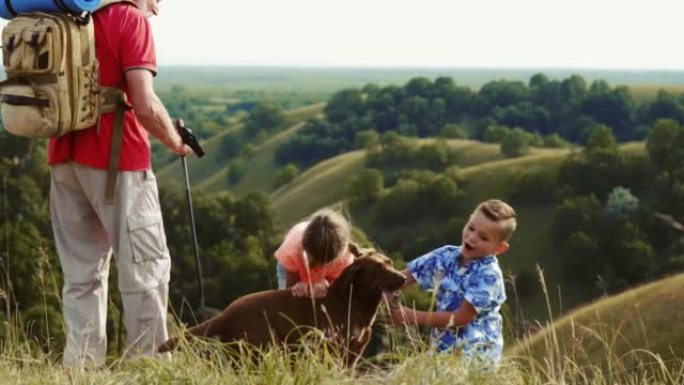 孩子们和祖父和他们的宠物狗在山顶上玩耍。家庭旅行概念