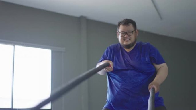 4k超重男子在健身房用战斗绳锻炼。