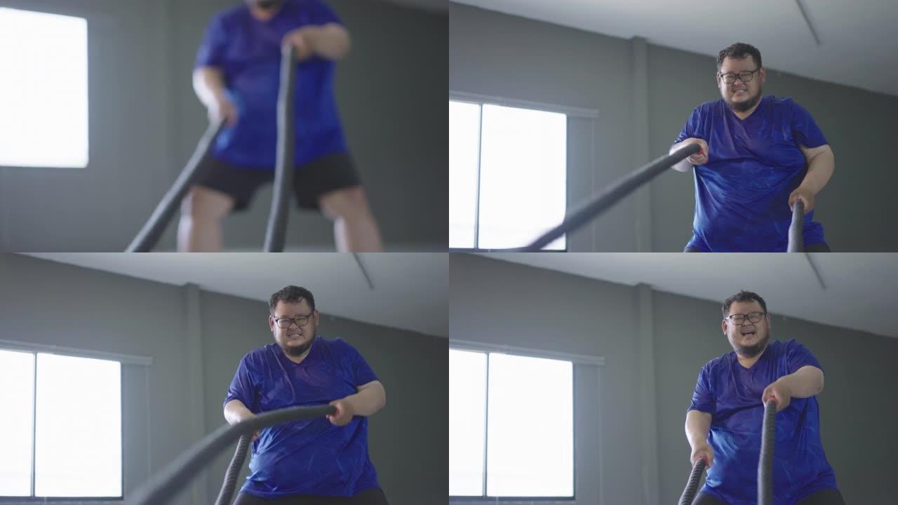 4k超重男子在健身房用战斗绳锻炼。