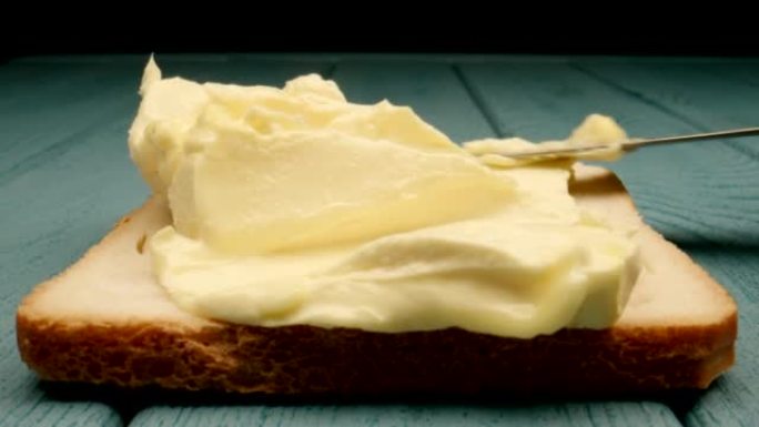 宏观: 大块黄油用小刀铺在蓝色木质背景上的面包上