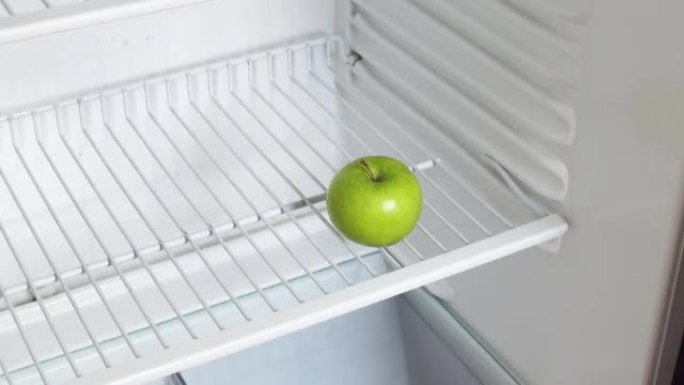 一个人的手打开一个空冰箱，拿了一个青苹果。概念性4k原始视频。经济危机、粮食短缺、贫困的想法。