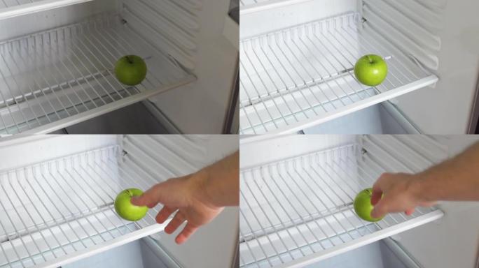 一个人的手打开一个空冰箱，拿了一个青苹果。概念性4k原始视频。经济危机、粮食短缺、贫困的想法。