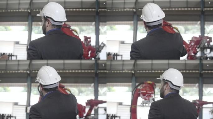 Sernior工程师在机器人手臂在后台移动的情况下在工厂内部查看和检查机器