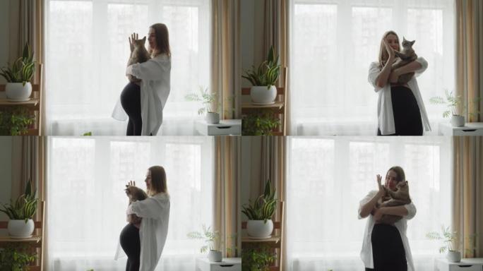 快乐孕妇在家里窗户附近抱着猫跳舞