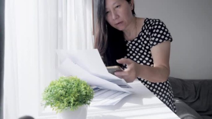 亚洲成年女性在家使用手机在窗口附近付款，财务概念。