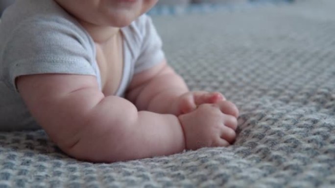 穿着灰色衣服的婴儿躺在床上，微笑着。婴儿的嘴和手的特写视图。婴儿护理。生命第一年的儿童发展