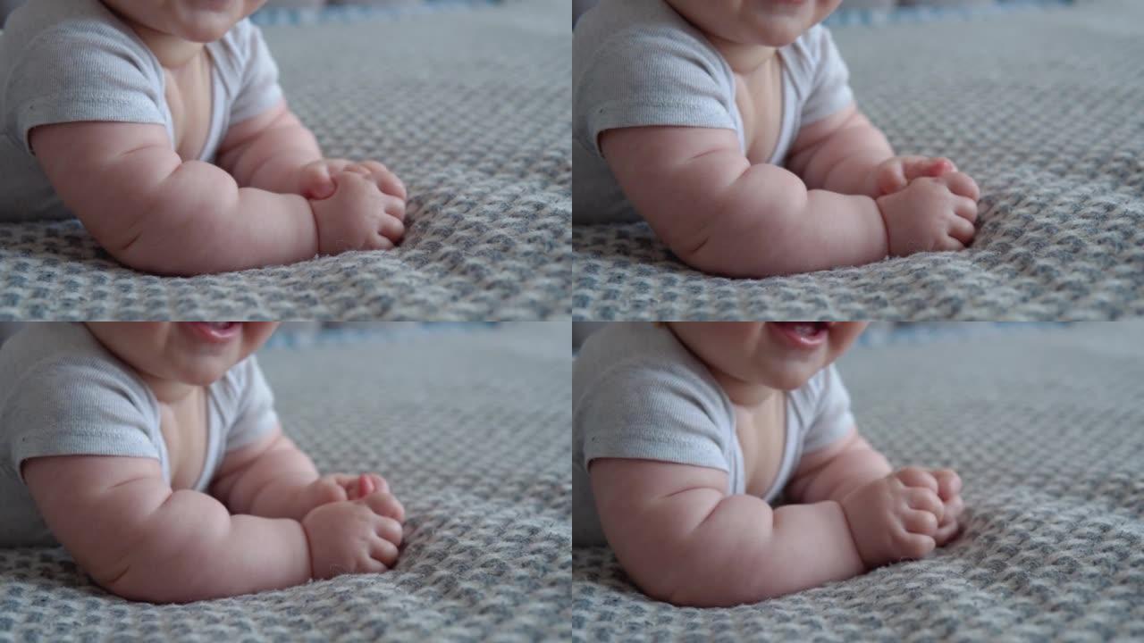 穿着灰色衣服的婴儿躺在床上，微笑着。婴儿的嘴和手的特写视图。婴儿护理。生命第一年的儿童发展