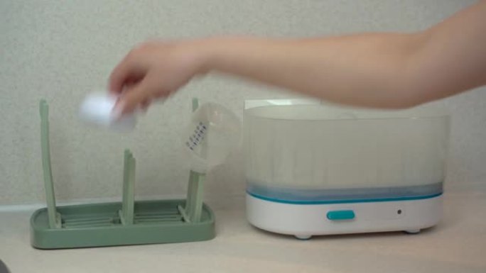 一名妇女从蒸汽消毒器中取出儿童餐具，然后将其挂在烘干机上。消毒器清洁细菌和细菌。