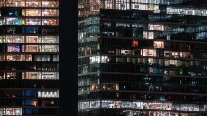 商务中心建筑立面的办公窗灯延时闪烁，人们深夜工作。公司业务，高摩天大楼玻璃表面。建筑窗户中的灯打开和