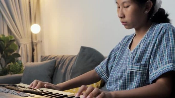 穿着睡衣的亚洲女孩在晚上在家的沙发上通过移动应用学习弹奏键盘乐器，生活方式概念。