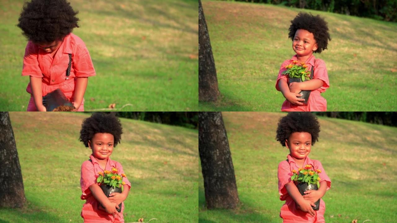一个快乐的美国非洲裔小男孩，手里拿着小花树，在绿色的大花园里欢快地跳舞。儿童夏季户外活动。感受快乐户