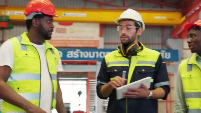 穿着制服的男工程师工作人员戴着安全安全帽，拿着平板电脑和剪贴板走路，向工业施工现场的同事解释工业工作
