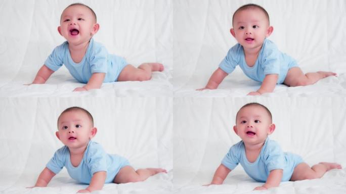 幸福的家庭，可爱的亚洲新生婴儿穿着蓝色衬衫躺着，在床上爬行玩耍，看着相机笑着笑脸。天真的小新婴儿可爱